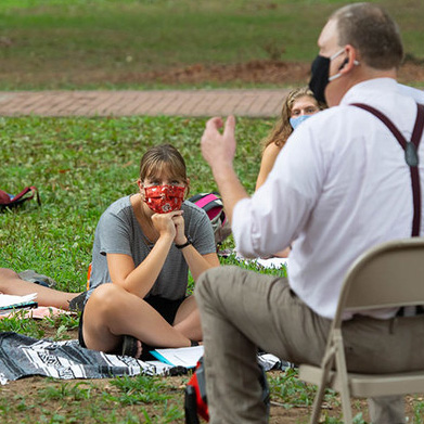 Faculty member in masks teaching outside in the grass